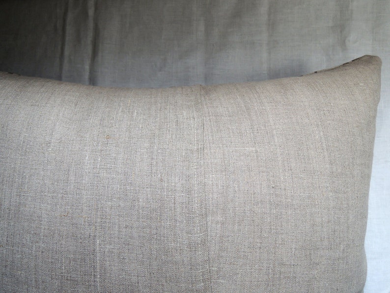 May include: A plain, light gray linen pillow with a subtle texture. The pillow is made of natural fabric and has a simple, understated design.