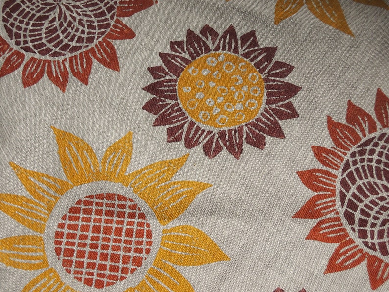 Puede incluir: Una tela beige con un patr&oacute;n repetitivo de girasoles marrones y naranjas. Los girasoles son estilizados y tienen un dise&ntilde;o geom&eacute;trico.