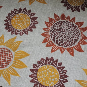 Puede incluir: Primer plano de una tela con un patr&oacute;n repetitivo de girasoles estilizados en tonos naranja, amarillo, marr&oacute;n y rojo. La tela tiene una textura similar al lino.