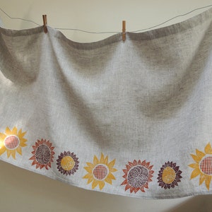 May include: A gray linen tablecloth with a border of printed sunflowers in shades of yellow, orange, and brown.
