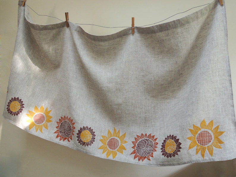 May include: A gray linen tablecloth with a border of printed sunflowers in shades of yellow, orange, and brown.