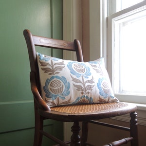 May include: A wooden chair with a woven seat and a blue and brown patterned pillow. The chair is in front of a green wall and a window.