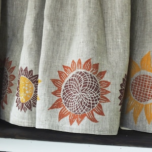 May include: A linen curtain with a brown, orange, and yellow sunflower print. The curtain has a simple, rustic design.