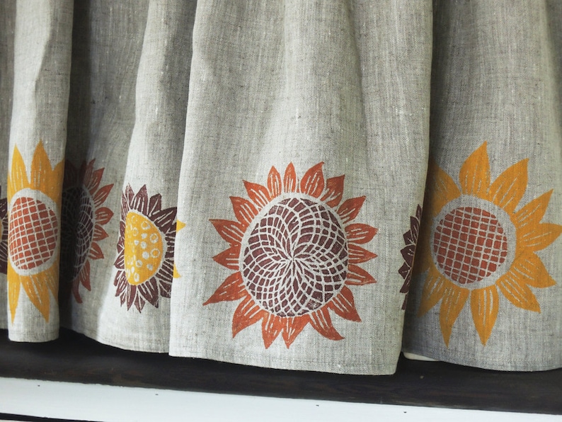 May include: A linen curtain with a brown, orange, and yellow sunflower print. The curtain has a simple, rustic design.