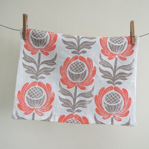 May include: A white tea towel with a repeating pattern of stylized flowers in shades of gray and coral.
