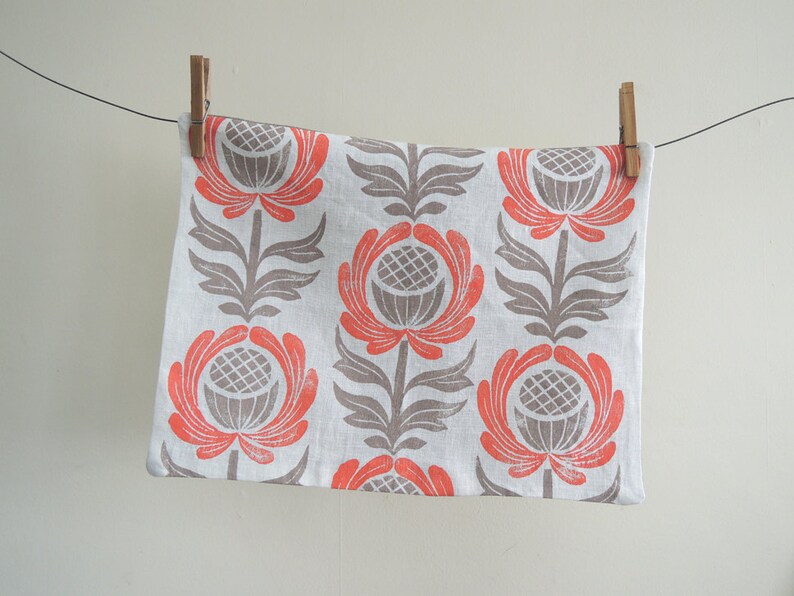 May include: A white tea towel with a repeating pattern of stylized flowers in shades of gray and coral.