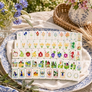 May include: A set of rectangular mahjong tiles featuring colourful illustrations of flowers, fruits, farm landscapes, and seasonal scenes. Each tile displays a unique graphic, including numbered floral arrangements, wheat stalks, fruits, and labelled directional markers.