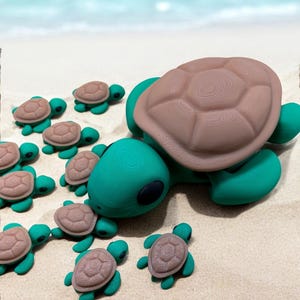 May include: A group of green and brown turtle figurines on a sandy beach. The largest turtle is facing the camera with its head down, as if it is leading the smaller turtles.