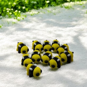May include: A group of 12 small, yellow and black bee figurines. The bees are made of a soft, rubbery material and have a 3D design.
