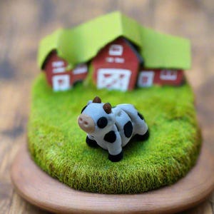May include: A miniature farm scene with a small red barn, green grass, and a black and white cow figurine.
