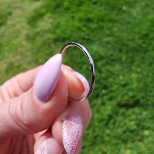 Puede incluir: Un fino anillo de banda de plata con un pequeño diamante engastado en el centro.