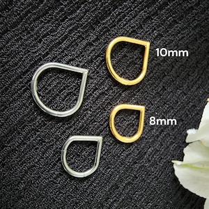 May include: Three teardrop-shaped metal rings in gold and silver. The gold rings are 8mm and 10mm in size. The silver ring is a similar shape. The rings are displayed on a textured black surface.