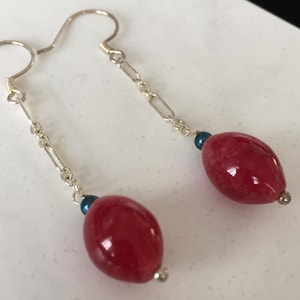 May include: A pair of silver earrings with red oval-shaped stones and blue accents.