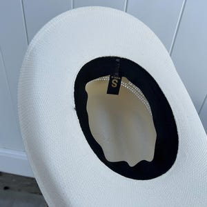 May include: A white straw hat with a black band around the crown. The hat has a size label that says "S" inside the band.