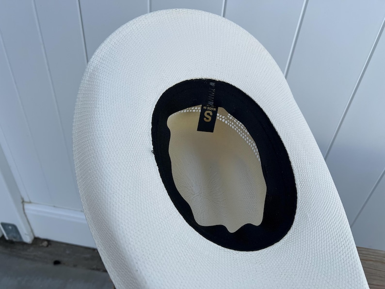 May include: A white straw hat with a black band around the crown. The hat has a size label that says "S" inside the band.