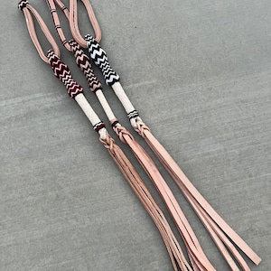 May include: Three leather braided whips with different colored braided handles. The handles are red and white, black and white, and white with a black and white pattern. The whips are all the same length and are laid out on a gray surface.