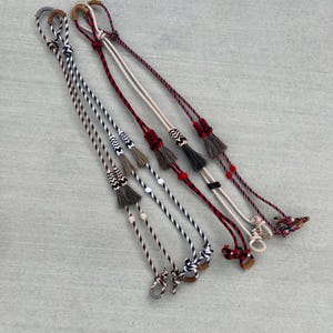 May include: Four braided leather reins with tassels and metal rings. The reins are black and white, red and white, and beige and brown.