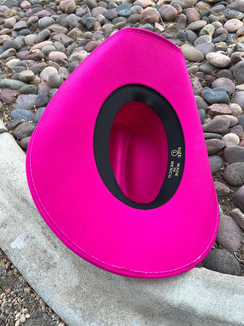 Puede incluir: Un sombrero de vaquero fucsia vibrante. El sombrero tiene un forro interior negro y una banda negra alrededor del borde interior. El sombrero est&aacute; hecho en M&eacute;xico y es talla L.