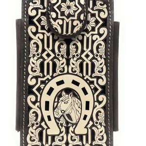 May include: A brown leather phone case with a decorative design. The case features a white horseshoe with a horse head, and an intricate floral and geometric pattern. The case has a magnetic closure.