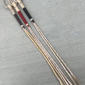 May include: Three leather whips with braided handles and long, thin, braided leather strands. The handles are black, brown, and red.
