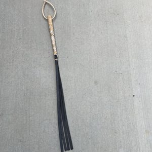May include: A braided leather whip with a black handle and a braided leather loop at the top.