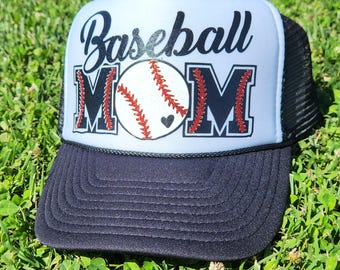 May include: A white and black baseball cap with a black mesh back. The front of the cap has the words "Baseball Mom" in black with a red baseball and a small red heart.