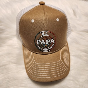May include: A brown and white trucker hat with a white logo that says "El Papa Mas Chingon" in a circle with a green, white, and red design inside the circle.