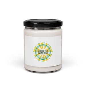 May include: A white candle in a glass jar with a black lid. The label features a circular design with the text "Cheers to a Clear Mind" in a teal and yellow color scheme. The candle is a home decor item.