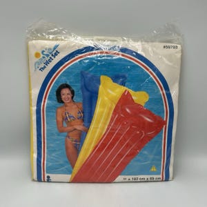 May include: An inflatable pool float in red, yellow, and blue, packaged in a clear plastic bag. The packaging features the text The Wet Set, model number #59703, and dimensions of 183 cm x 69 cm. A graphic shows a person in a bikini.