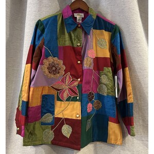 May include: A colorful patchwork button-down shirt with long sleeves. The shirt features a variety of colors, including red, blue, green, and yellow. It is decorated with embroidered floral designs and gold buttons.