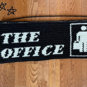 Può includere: Arazzo da parete in crochet bianco e nero con il testo "THE OFFICE" e un'immagine stilizzata di due persone sedute a una scrivania.