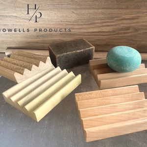 May include: Wooden soap dishes in various light wood tones, with a bar of soap and a round soap. The soap dishes have a slatted design to allow for drainage. The text "Howells Products" is at the top.