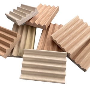 May include: A collection of wooden soap dishes in various shapes and shades of light brown. The dishes have a ridged design to allow for drainage. The wood grain is visible, and the dishes are arranged against a white background.