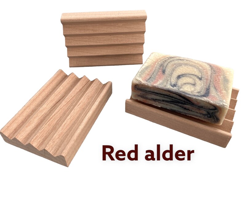 May include: Three red alder wood soap dishes. One dish holds a bar of soap with a marbled design in shades of red, blue, and white. The other two dishes are empty. The text "Red alder" is visible.