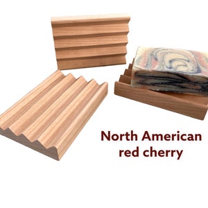 May include: Three wooden soap dishes made from North American red cherry wood. The soap dishes have a slatted design to allow for drainage. One dish holds a bar of soap with a marbled pattern.