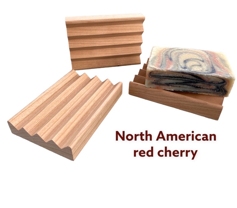May include: Three wooden soap dishes made from North American red cherry wood. The soap dishes have a slatted design to allow for drainage. One dish holds a bar of soap with a marbled pattern.