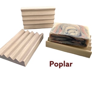 May include: Three poplar wood soap dishes with a grooved design. One dish holds a bar of soap with a marbled pattern of red, blue, and black. The word "Poplar" is printed in red.