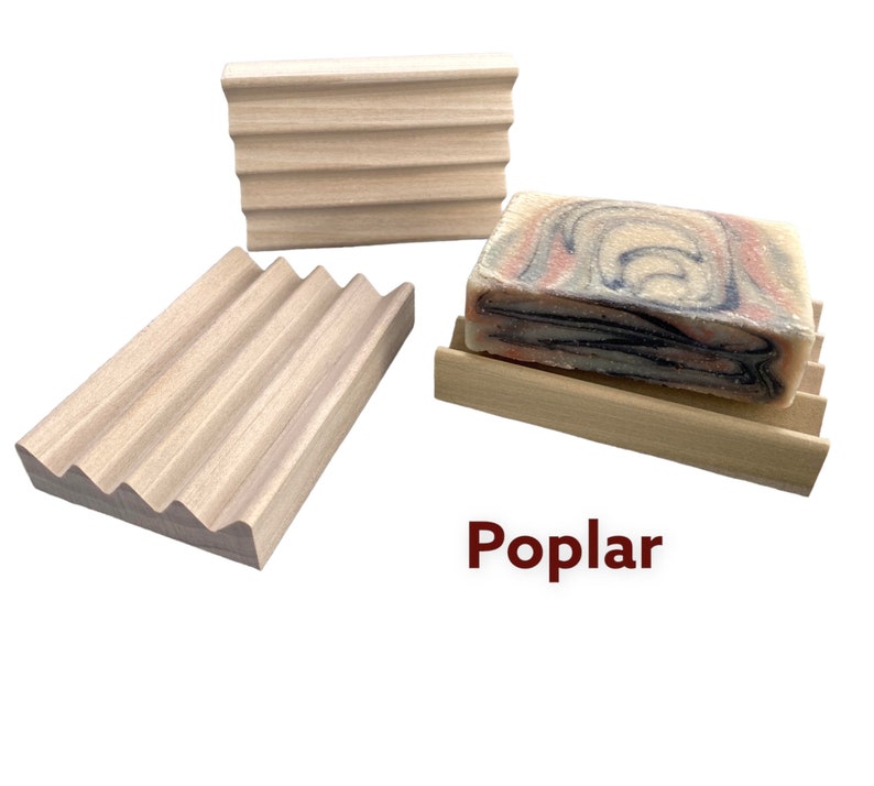 May include: Three poplar wood soap dishes with a grooved design. One dish holds a bar of soap with a marbled pattern of red, blue, and black. The word "Poplar" is printed in red.
