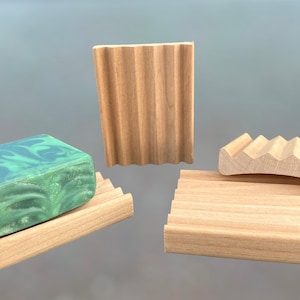 May include: Three wooden soap dishes with a ribbed design. One dish has a bar of green and white marbled soap on top.