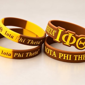 May include: Three silicone wristbands in brown and yellow. Two bands feature the text Iota Phi Theta and the Greek letters IΦΘ. One band is brown with yellow embossed Greek letters IΦΘ and the text IOTA PHI THETA in yellow lettering.
