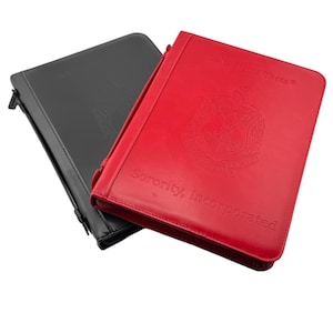 May include: Two leather-bound binders, one red and one black. The red binder has the text "Delta Sigma Theta Sorority, Incorporated" and a crest with the Greek letters "DST" embossed on the front.