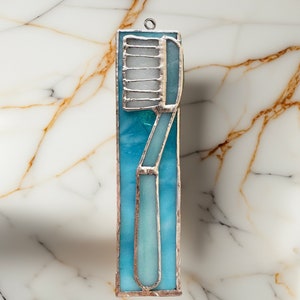 May include: A stained glass window hanging ornament depicting a toothbrush in shades of blue and white.