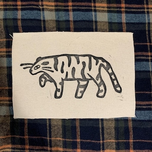Può includere: Un'illustrazione in bianco e nero di una tigre su un pezzo di tela bianca. La tigre cammina verso destra e ha un motivo a strisce.