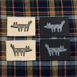 May include: Four fabric patches with a stylized black and white wolf design. Two patches are on a white background and two patches are on a black background.