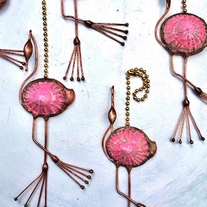 May include: Four pink flamingo-shaped metal fan pulls with gold chains. The flamingoes have a textured pink finish and are suspended from the chains.
