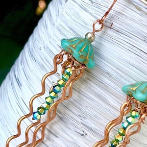 May include: Copper wire earrings with a turquoise blue glass jellyfish charm and iridescent green crystal beads.