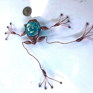 May include: A copper frog sculpture with a turquoise glass body and outstretched legs. The frog's body is made of copper, and the legs are wire. A coin is next to the frog for size comparison.