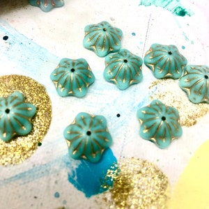 May include: A collection of teal blue star-shaped beads with gold accents. The beads have a raised design and a small hole in the center.