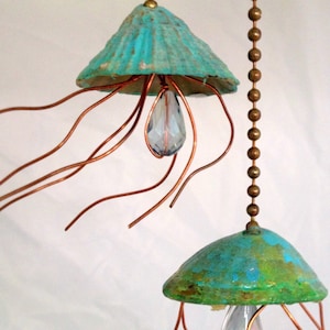 May include: Two teal blue and green shell-shaped hanging ornaments with copper wire tentacles and crystal drops. The ornaments are suspended from a chain.
