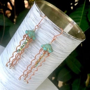 May include: Copper wire earrings with a turquoise and green shell-shaped charm and crystal beads dangling from the bottom.